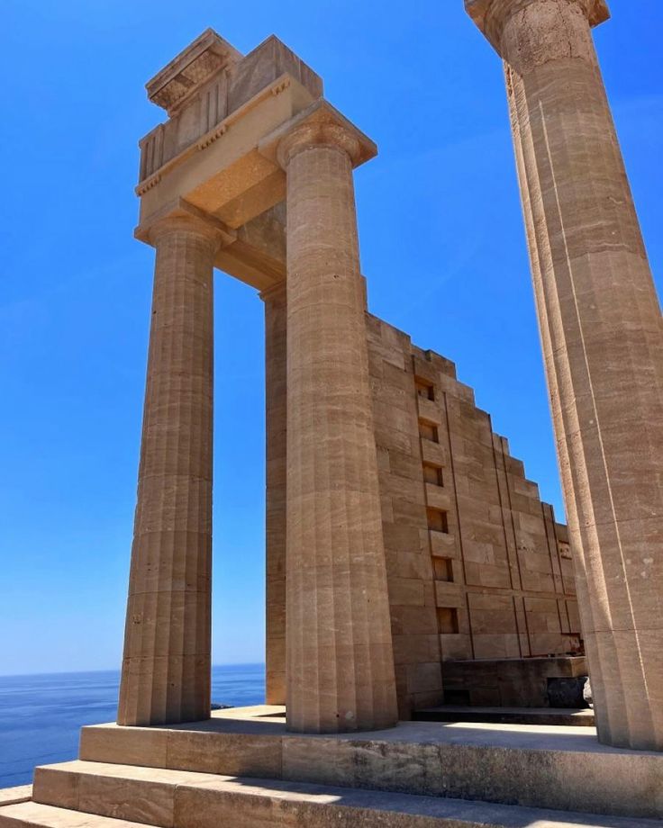 two large stone pillars sitting next to each other in front of the ocean on a sunny day