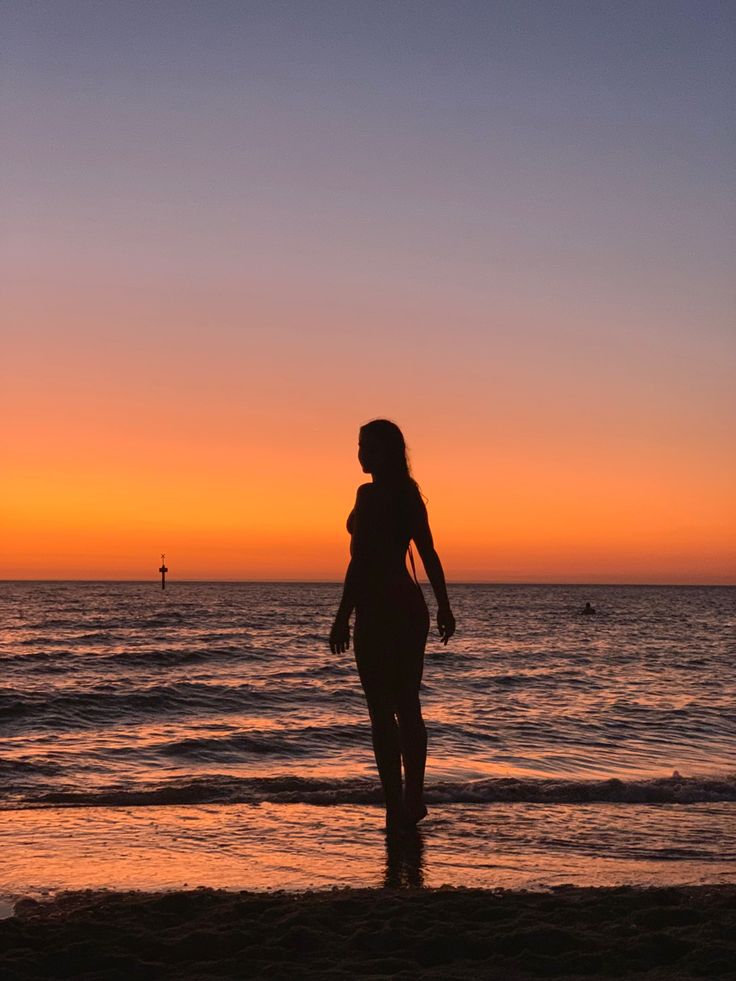 a woman standing on top of a beach next to the ocean at sunset or dawn