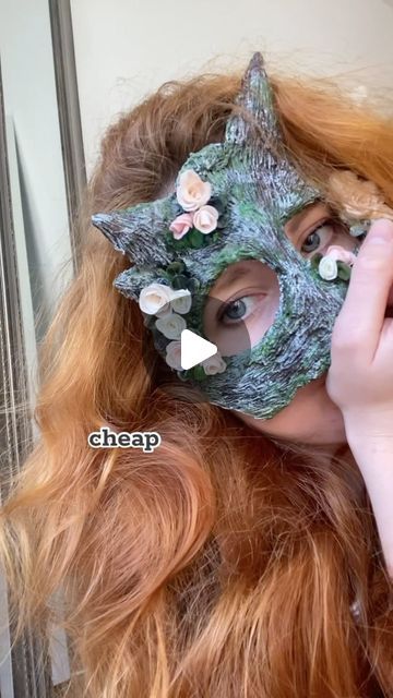 a woman with long red hair wearing a green mask and holding her face to the side