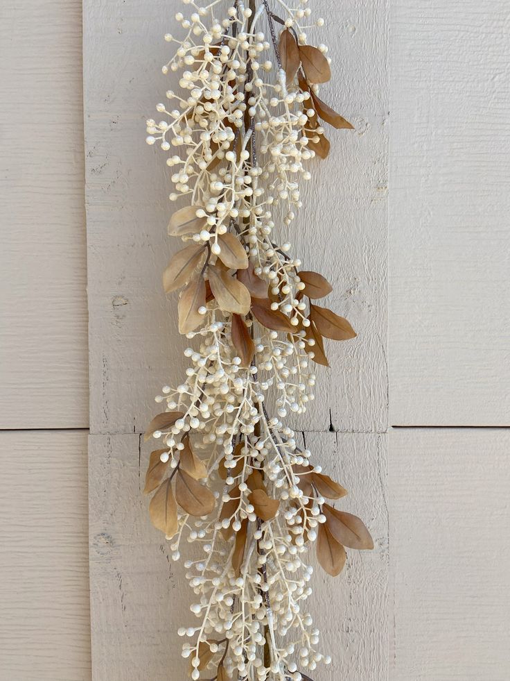 some white flowers and brown leaves hanging on a wall