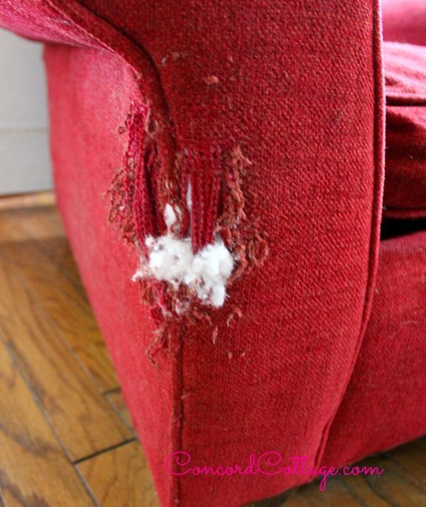 a red couch that has been torn apart and is sitting on a wooden floor with a hole in it