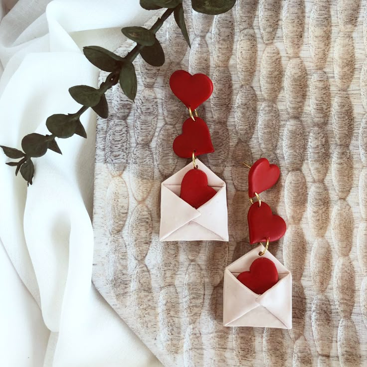 two red hearts are attached to white origami envelopes with gold earwires