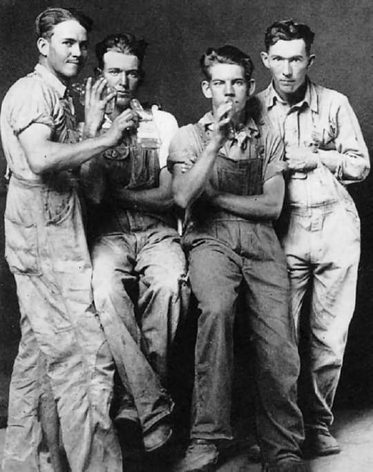 an old black and white photo of four men in overalls posing for the camera