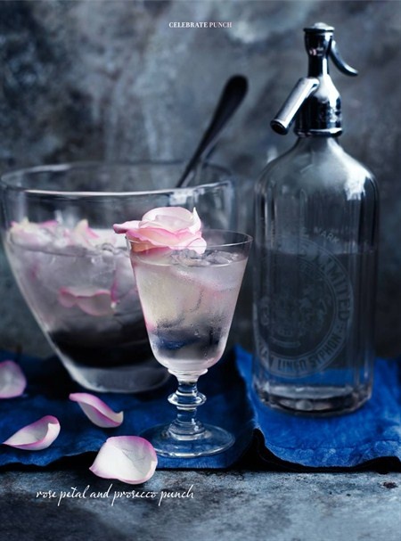 two glasses filled with ice and rose petals next to a bottle of alcohol on a blue towel