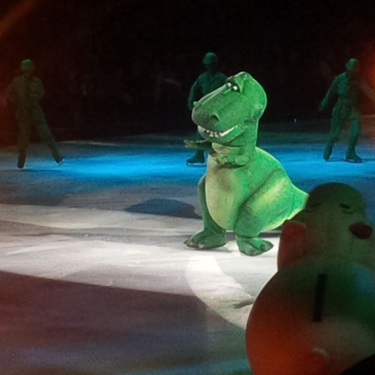 an inflatable dinosaur is standing on the ice with other people behind it at night