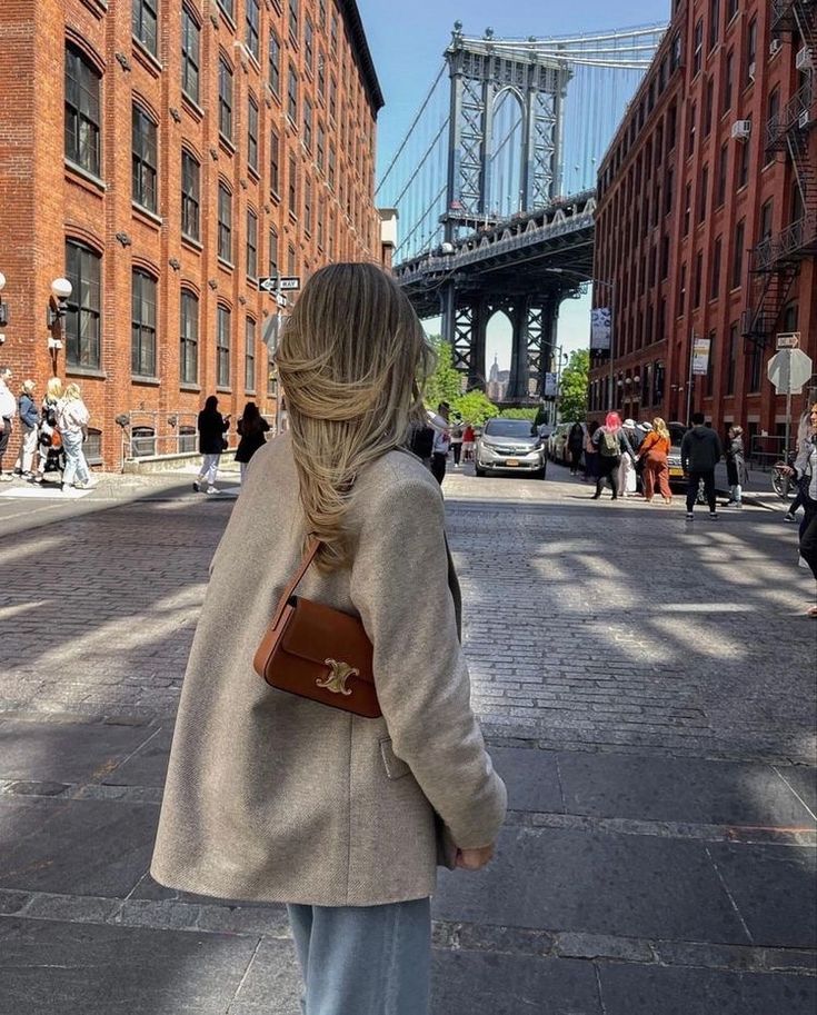 a woman is walking down the street in front of some tall buildings and a bridge