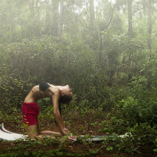 a woman kneeling down in the woods on her yoga mat