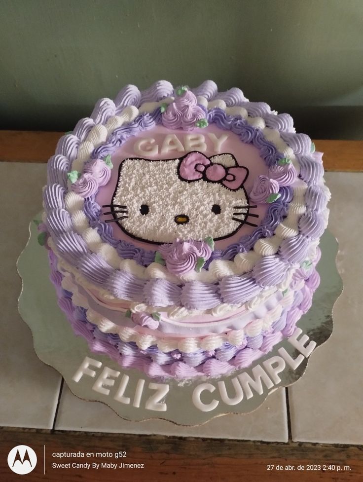 a hello kitty cake with purple icing and white frosting on the top, sitting on a tile floor