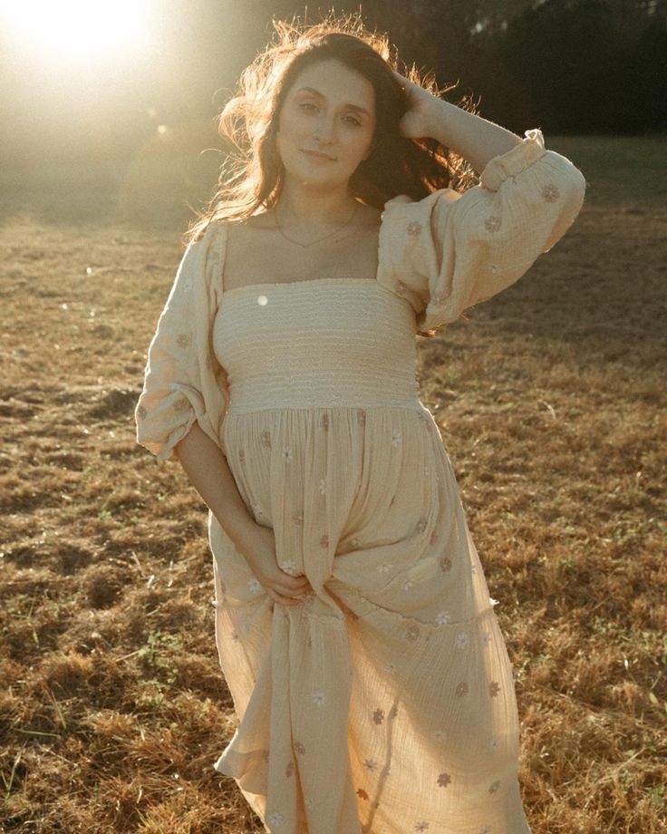 a woman standing in a field with her hands on her head and the sun shining behind her