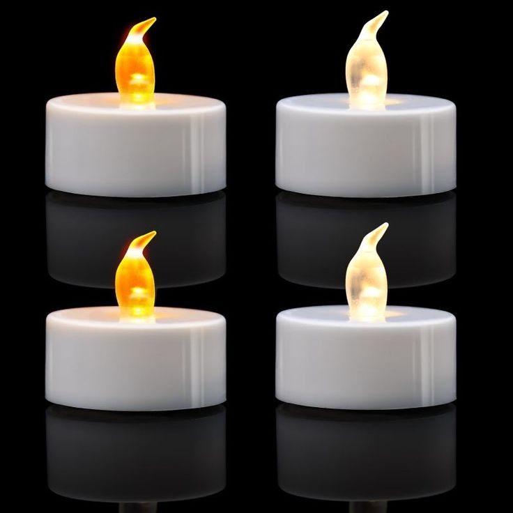 three lit candles sitting side by side on a black surface with reflections in the dark