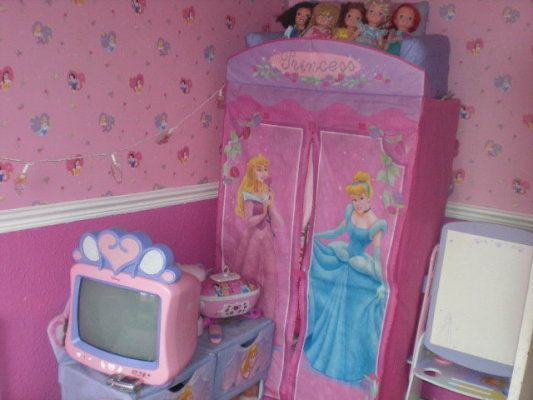 a pink princess themed bedroom with toys on the dresser and tv in the corner next to it