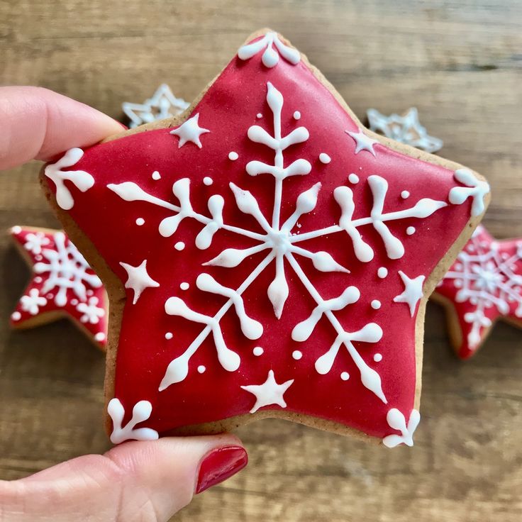 a hand holding a red and white decorated star shaped cookie on top of a wooden table