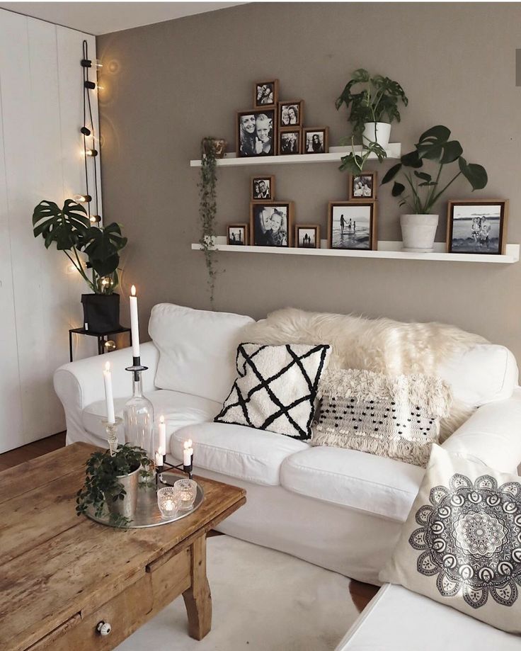 a living room filled with white furniture and lots of greenery on the shelves above