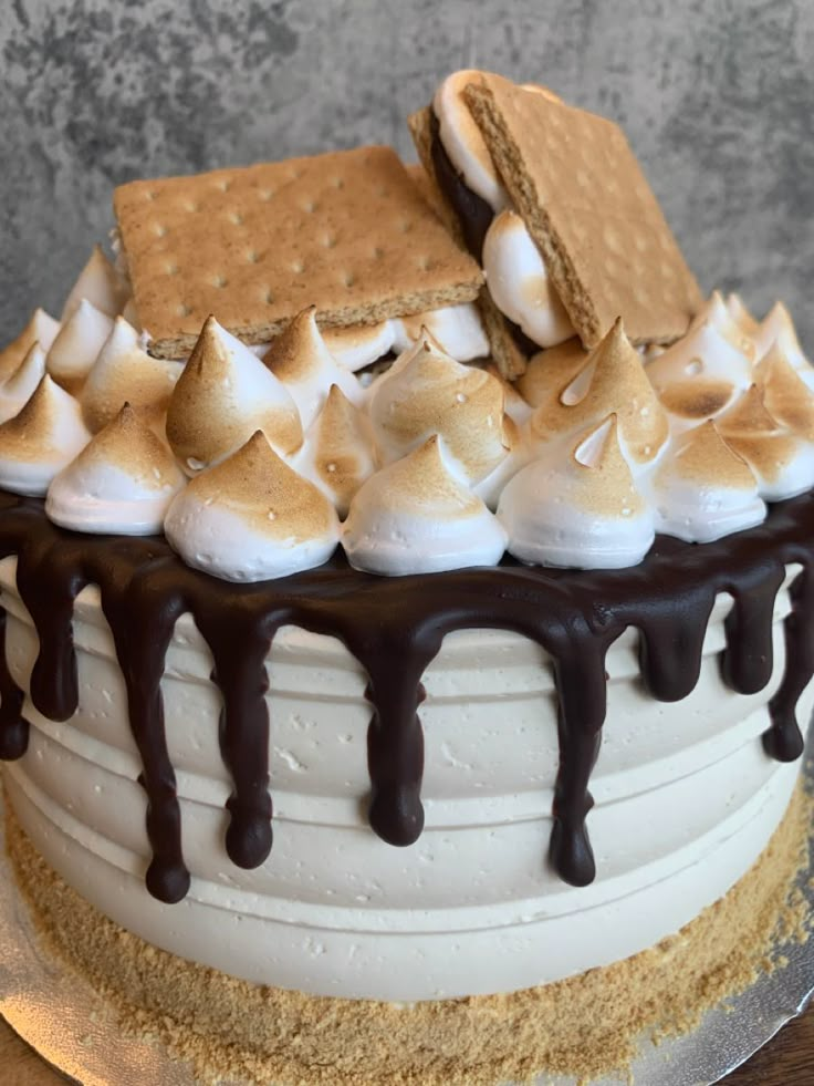 a cake with white frosting and chocolate drizzled on top, topped with marshmallows