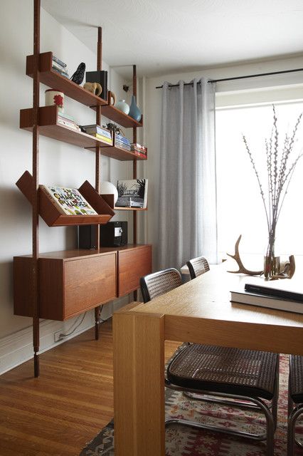 a room with a table, bookshelf and chairs next to a large window