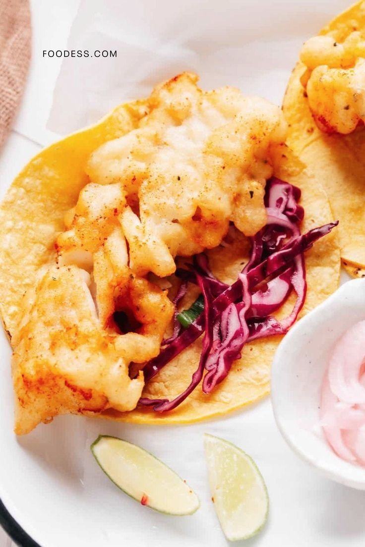 two fish tacos with cole slaw and sour cream sauce on a white plate