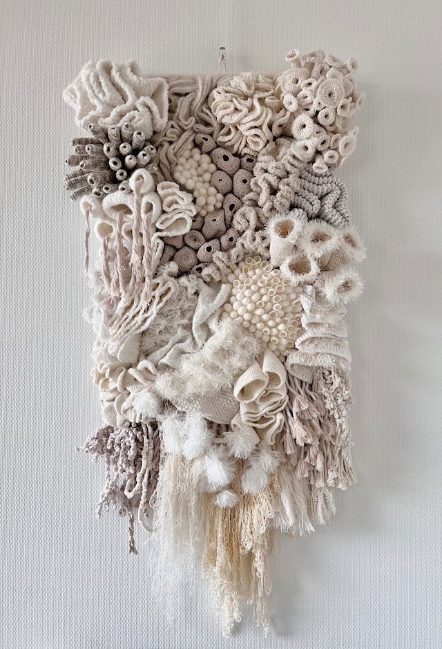 a wall hanging made out of different types of fabric and beads on a white wall