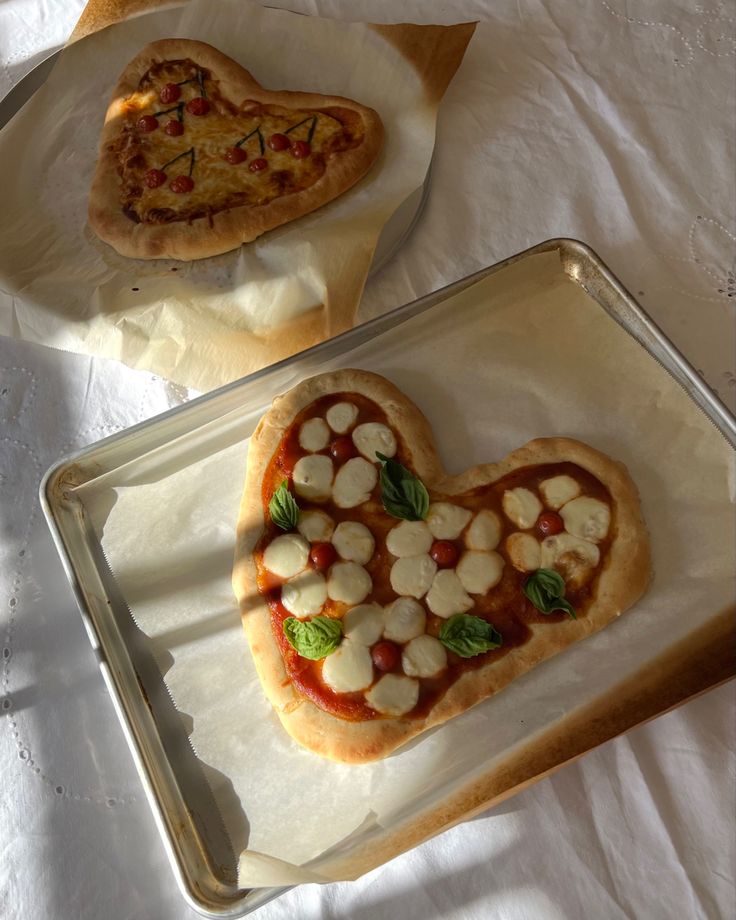 two heart shaped pizzas sitting on top of pans next to each other with toppings