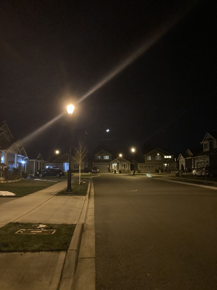 an empty street at night with lights on and houses in the backgrouds