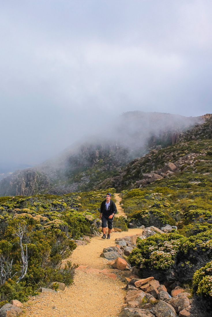 a man walking down a trail in the mountains on a foggy day with low clouds