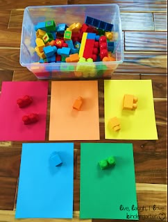 legos are sitting on top of colored paper in front of a plastic container filled with blocks