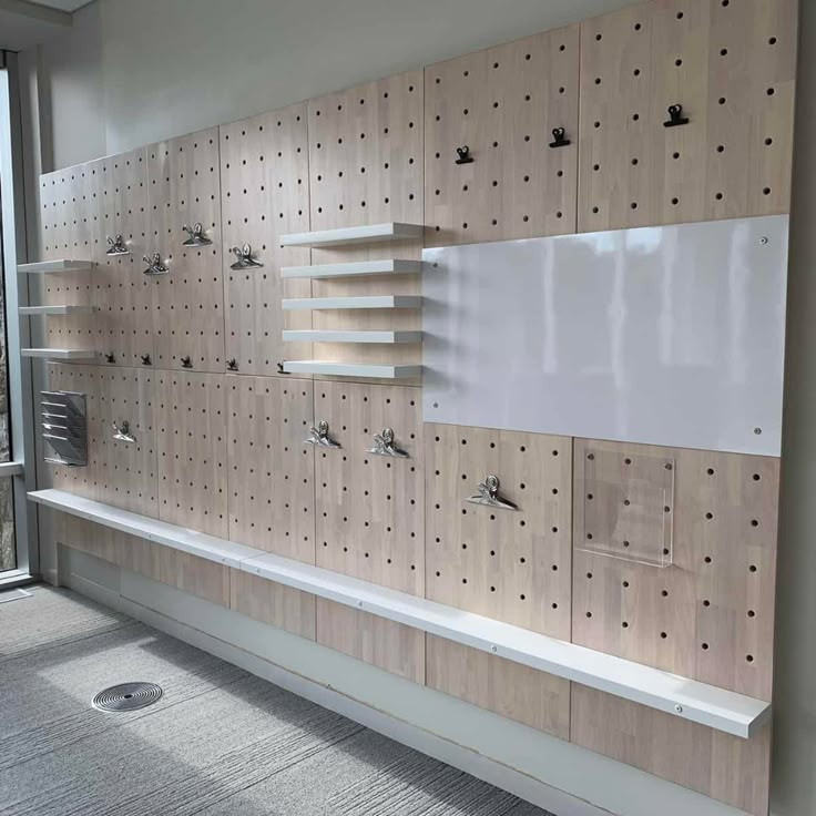 a room with wooden pegboard on the wall and shelves in front of large windows