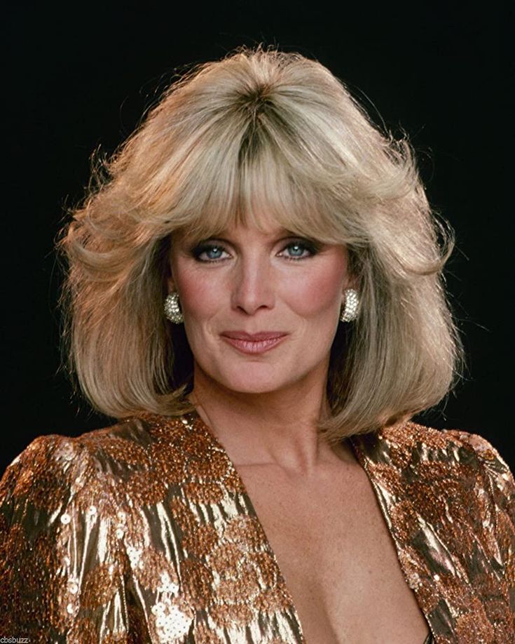 an older woman with blonde hair and blue eyes wearing a gold dress in front of a black background