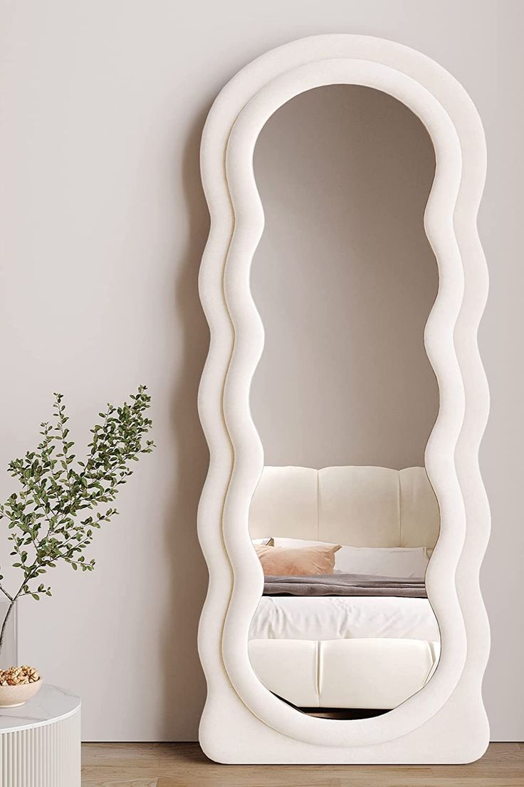 a large white mirror sitting on top of a wooden floor next to a vase filled with flowers