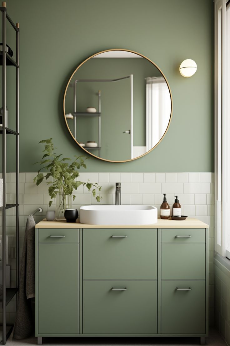 a bathroom with green cabinets and a round mirror above the sink, along with a plant