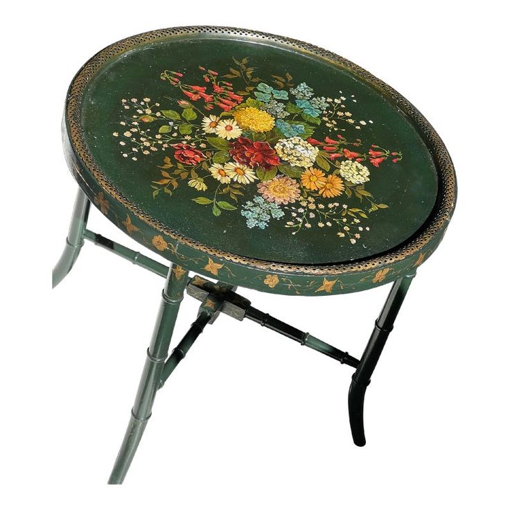 a small green table with flowers painted on the top and metal legs, sitting in front of a white background