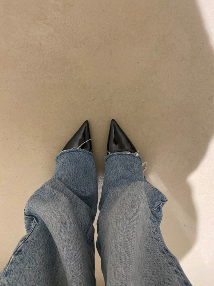 a person's feet in jeans and black shoes, with their legs tucked into the floor