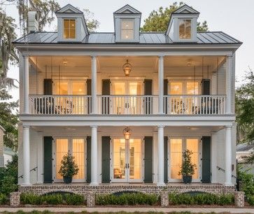 a white house with green shutters on the front and second story, surrounded by trees