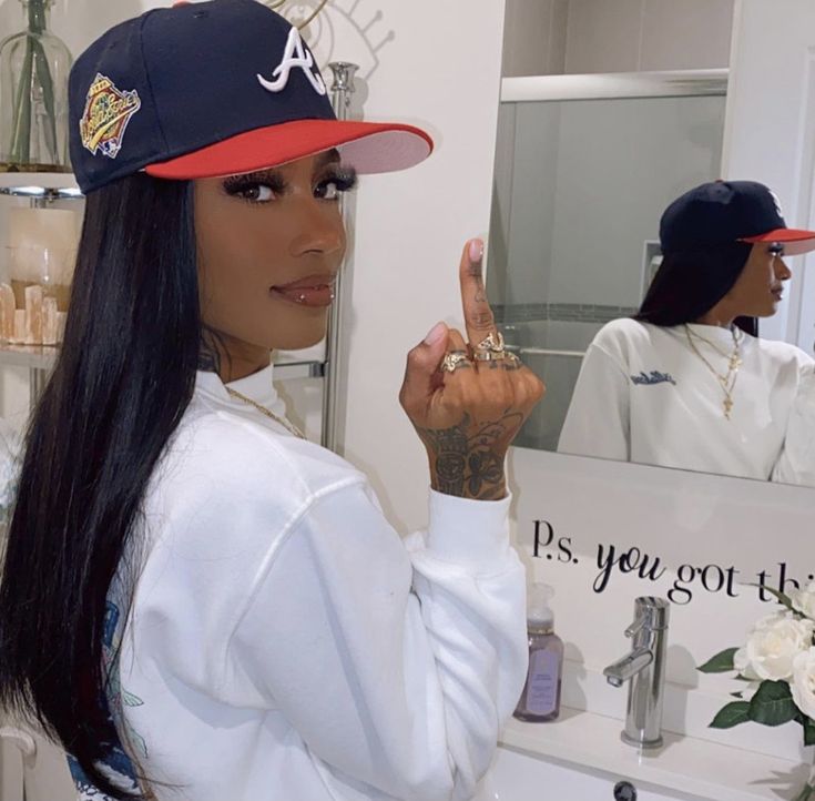 a woman with long black hair wearing a hat and making the peace sign in front of a mirror