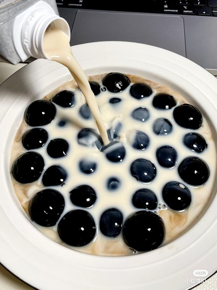 a person pouring milk into a bowl filled with black and white liquid on top of a laptop