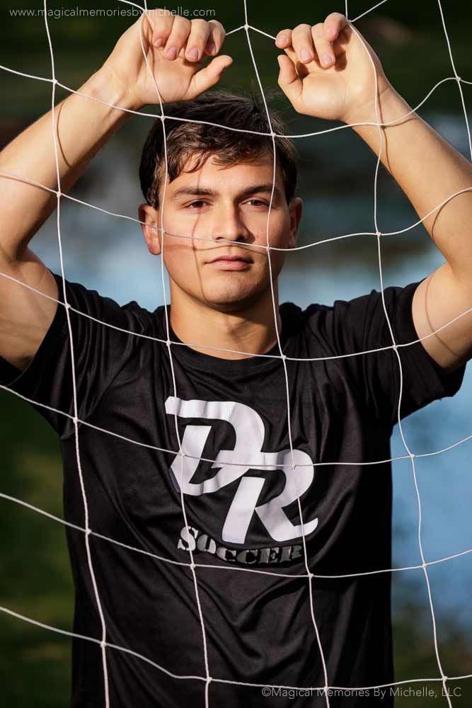 a man standing behind a soccer net holding his hands up to his head and looking at the camera