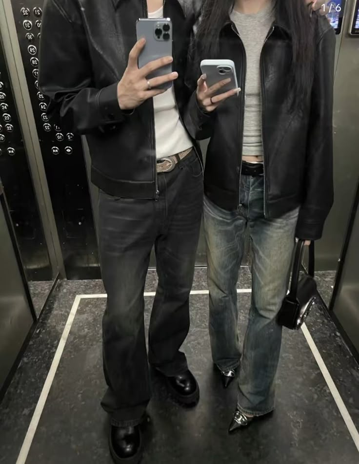 two people standing next to each other in front of elevators holding cell phones and looking at the camera