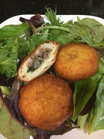 two fried meat patties on top of a green salad with lettuce and leafy greens