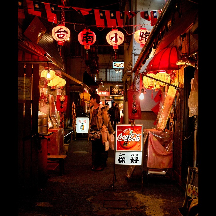 people walking through an alley at night with chinese lanterns hanging from the ceiling and signs above them