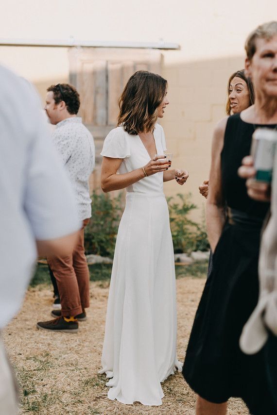 a woman in a white dress standing next to other people and looking at her phone