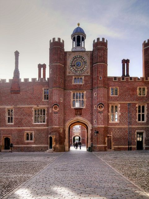 a large brick building with a clock on it's face and two people walking in the doorway