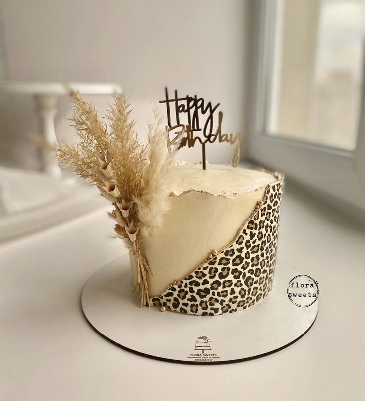 a leopard print cake with a happy birthday topper and some dry grass on it