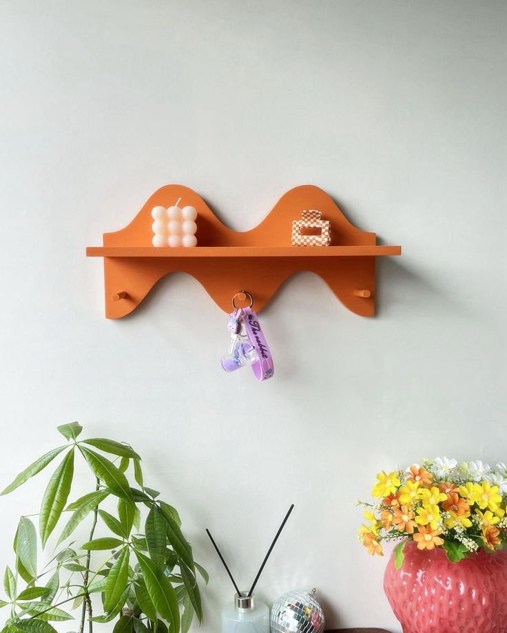 an orange shelf on the wall above a vase with flowers