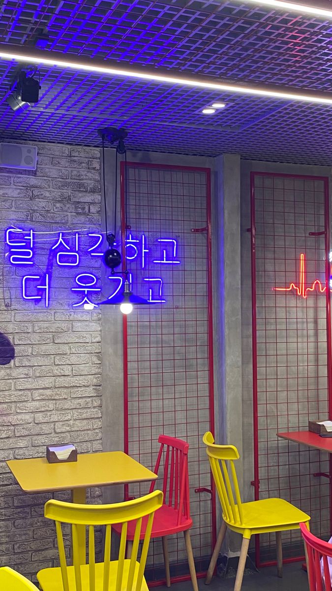 the interior of a restaurant with bright colored chairs and neon signs on the wall above them