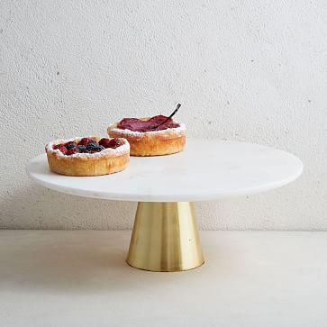 two pastries sitting on top of a white cake plate next to each other in front of a white wall