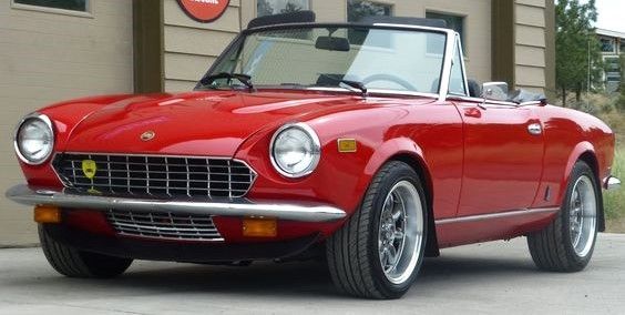 an old red sports car parked in front of a building with a sign on it