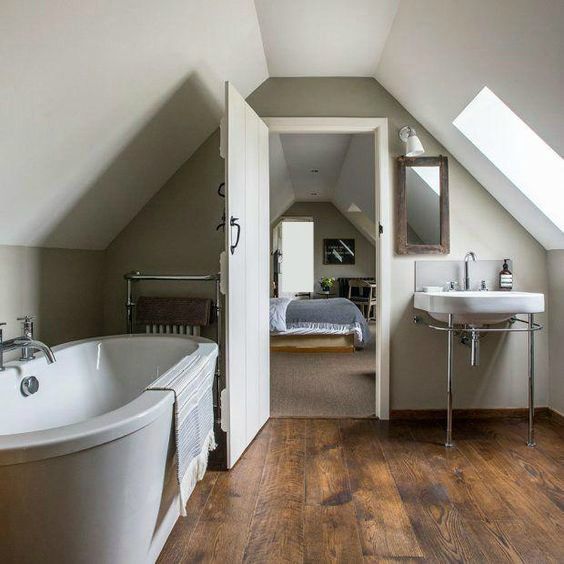 a bathroom with a tub, sink and mirror in the corner next to an attic bedroom