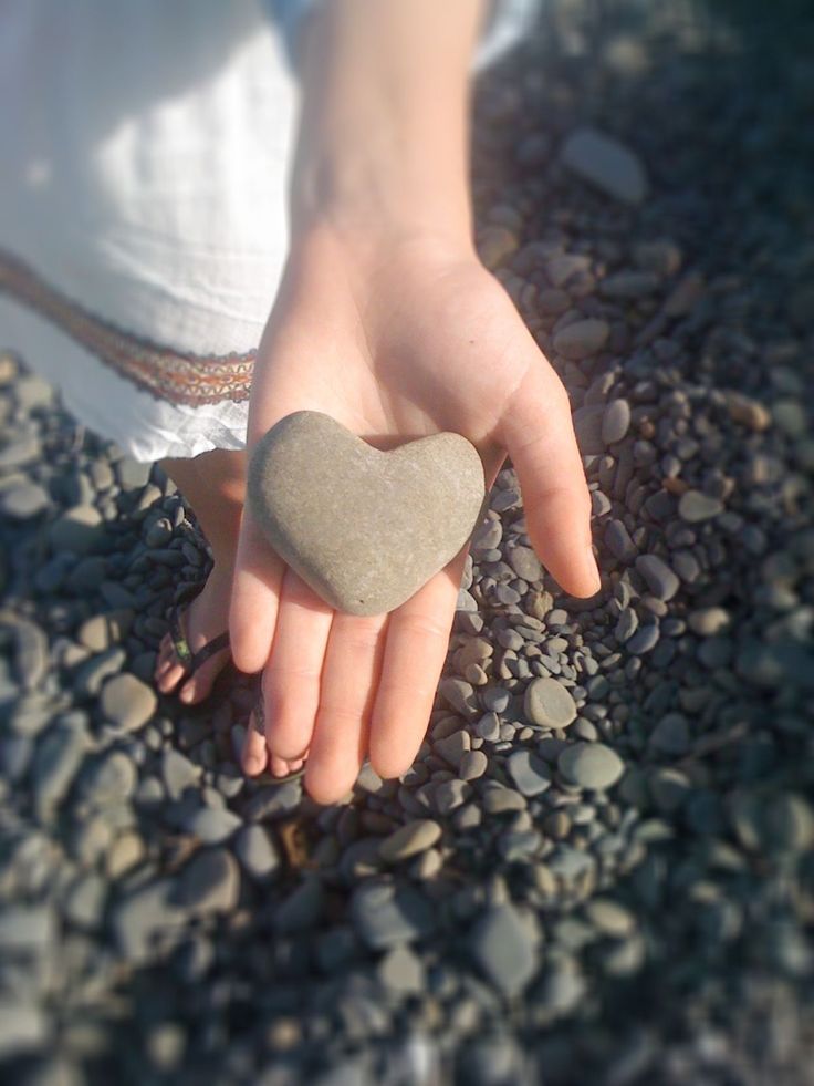 a person holding a heart shaped rock in their hand on some rocks and gravel,