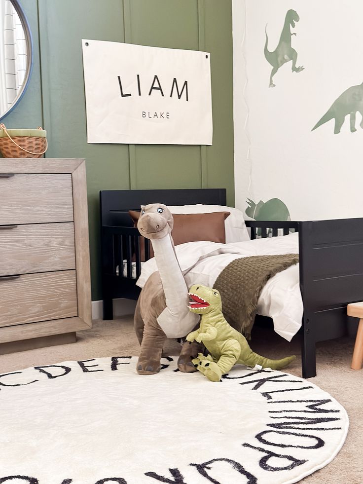 two stuffed dinosaurs sitting on the floor in a child's bedroom with green walls