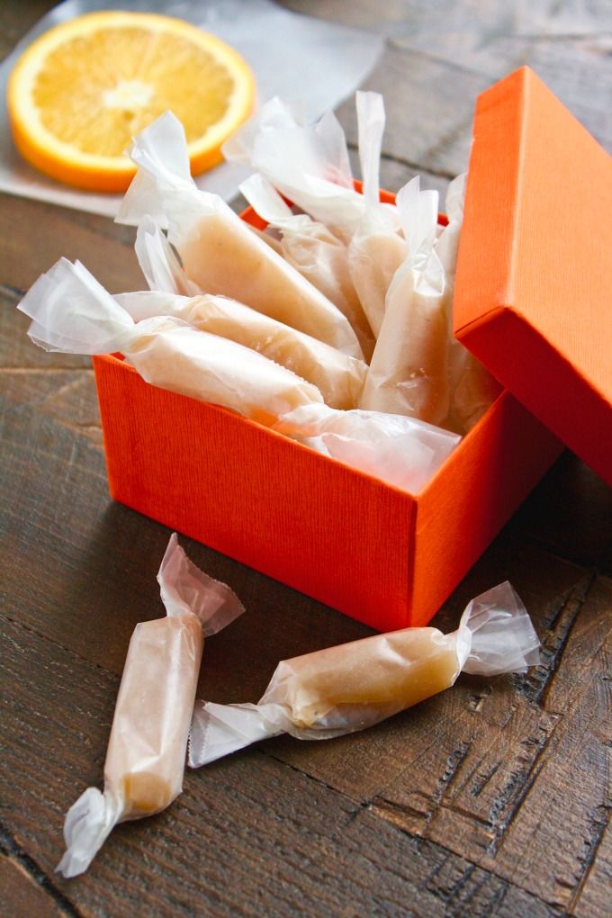 an orange box filled with candy sitting on top of a wooden table next to an orange slice