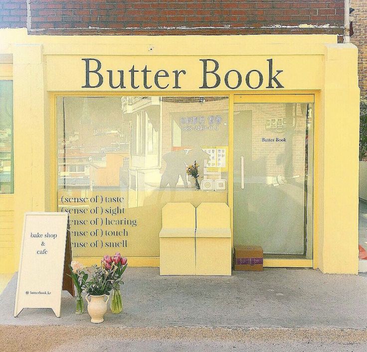 a yellow store front with flowers in the window and a sign on the sidewalk that says butter book